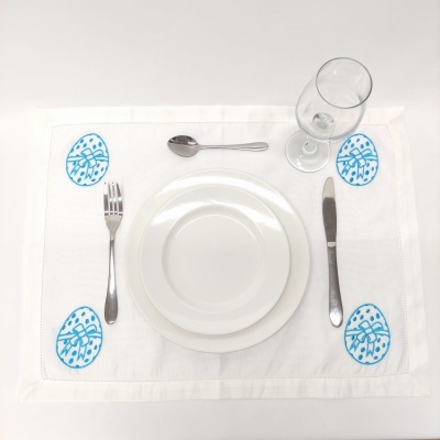 Lugar de mesa com pratos brancos, talheres, taça e individual com ovos azuis