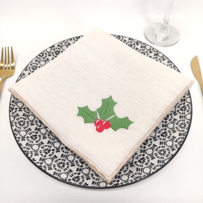 Guardanapo branco com bordado de folhas verdes e bagas vermelhas sobre prato decorado preto e branco