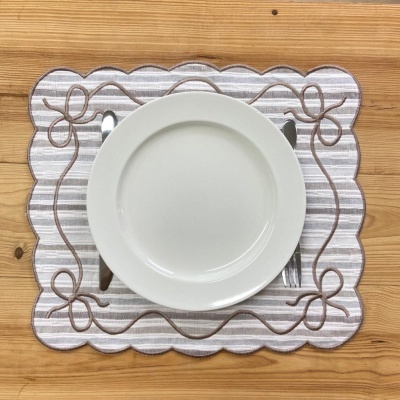 Jogo americano com padrão riscado cinza e branco e decorado com laços castanhos, prato branco e talheres sobre mesa de madeira.