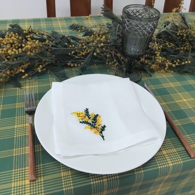 Mesa posta com prato branco, guardanapo bordado, copo cinza e talheres de cabo de madeira sobre toalha xadrez verde e amarelo