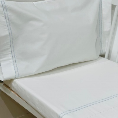 Conjunto de roupa de cama branca com costura azul numa cama branca