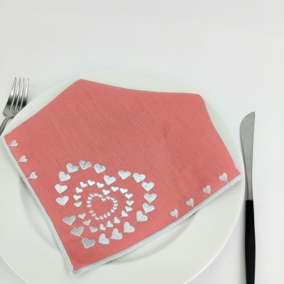 Guardanapo cor de salmão com corações brancos, prato branco, talheres ao lado