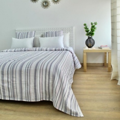 Quarto com cama de casal e roupa de cama às riscas, mesa de cabeceira com vaso e planta, cortinas brancas