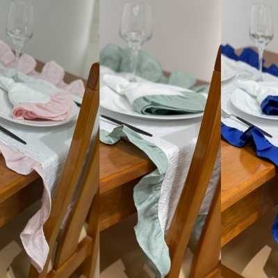 Três mesas postas com pratos brancos, copos e toalhas com bordas onduladas coloridas