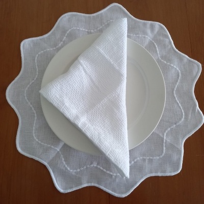 Conjunto de mesa com prato branco, guardanapo branco dobrado e sousplat branco ondulado sobre madeira