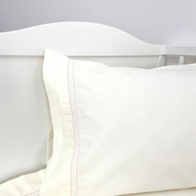 Fronha branca com costura vermelha sobre cama branca com cabeceira de madeira