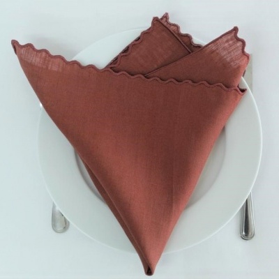 Guardanapo de tecido castanho dobrado sobre prato branco com talheres ao lado.