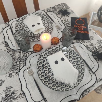 Mesa posta com pratos, guardanapos com olhos, velas, aranhas decorativas e livro temático