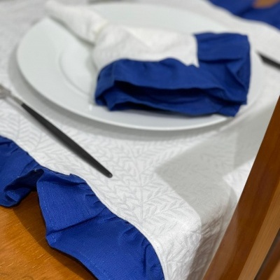 Toalha de mesa branca com borda azul e guardanapo branco e azul em prato branco sobre mesa de madeira