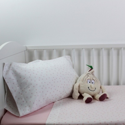 Cama de bebé com lençóis cor-de-rosa claro e peluche de alho sorridente
