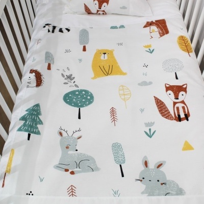 Lençol e fronha de berço branco com estampas de animais e árvores coloridas.