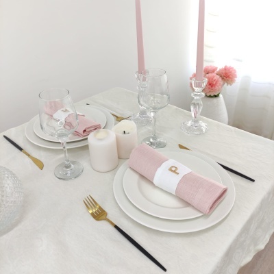 Mesa posta elegante com pratos brancos, copos transparentes, talheres pretos e dourados, guardanapos rosa e velas