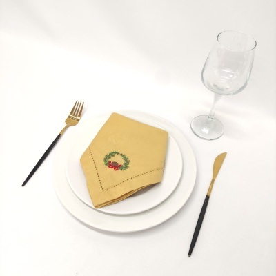 Conjunto de jantar com pratos brancos, guardanapo bege bordado, talheres pretos e dourados, taça de vidro