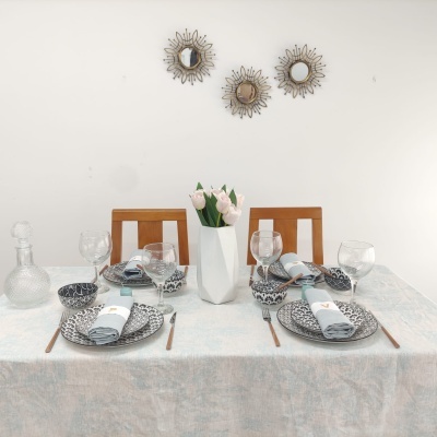 Mesa posta com pratos, taças, guardanapos cinza, talheres castanhos, vaso branco com flores e três espelhos redondos na parede