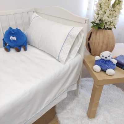 Cama branca com roupa de cama branca com detalhes em azul claro, peluches e mesa com vaso de flores