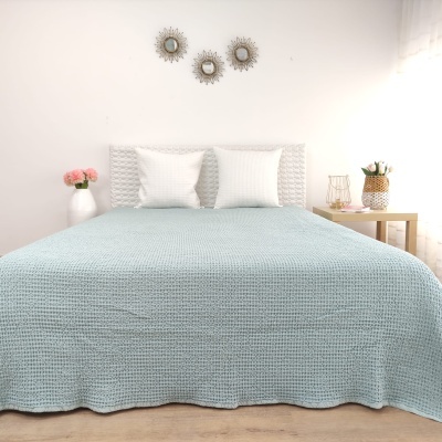 Cama com colcha azul clara texturada e decoração num quarto claro