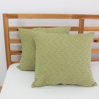 Par de almofadas verdes com textura acolchoada sobre estrado de madeira clara.