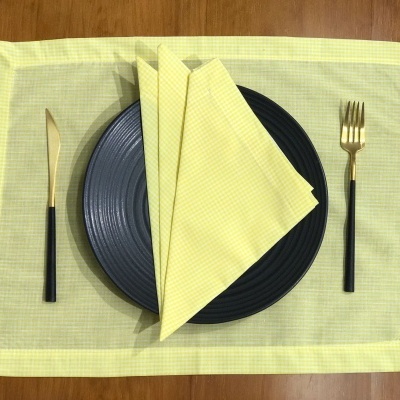 Mesa posta com individual e guardanapo amarelos, prato preto e talheres dourados e pretos