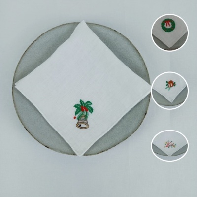 Guardanapos de tecido branco com bordados de Natal variados sobre prato cinzento