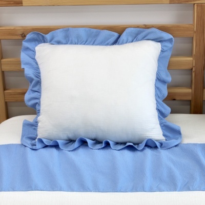 Almofada branca com babados azuis sobre cama com cabeceira de madeira