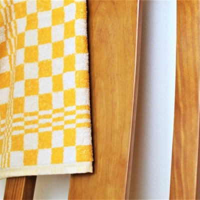 Toalha amarelo e branca pendurada numa cadeira de madeira clara