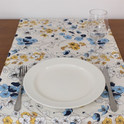 Mesa posta com toalhete floral, prato branco, talheres e copo de vidro