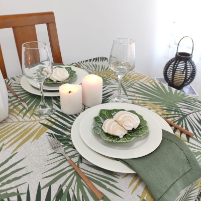 Mesa posta com conjunto de jantar, toalha e pratos com padrão de folhas verdes, e velas acesas.