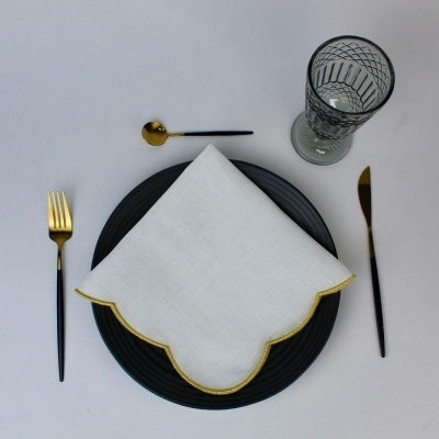 Conjunto de talheres dourados e pretos, prato preto, guardanapo branco com borda dourada, copo de vidro padrão geométrico