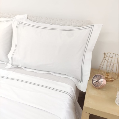 Jogo de cama branco com franjas cinza e acessórios numa mesa de cabeceira