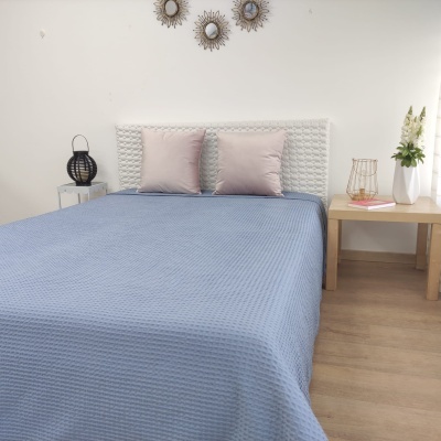 Cama com colcha azul e almofadas cor-de-rosa com mesas laterais decoradas