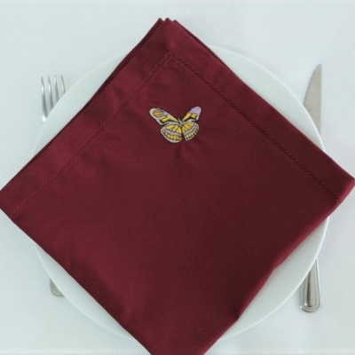 Guardanapo bordô com bordado de borboleta sobre prato branco e talheres.