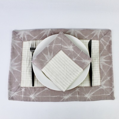 Individual retangular bege claro com estrelas brancas, guardanapo e suporte de talheres às riscas bege e branco, prato branco, garfo e faca.