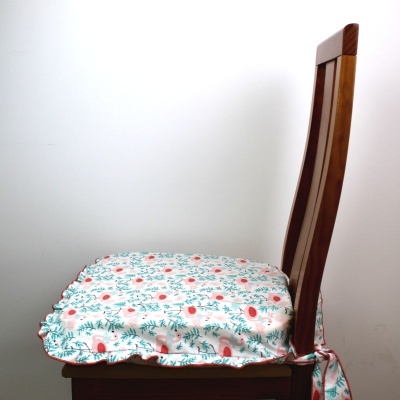 Capa acolchoada de cadeira com padrão floral em azul e coral, fixada a cadeira de madeira castanha