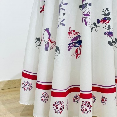 Tecido branco com padrão de pássaros coloridos e detalhes vermelhos pendurado como capa de mesa