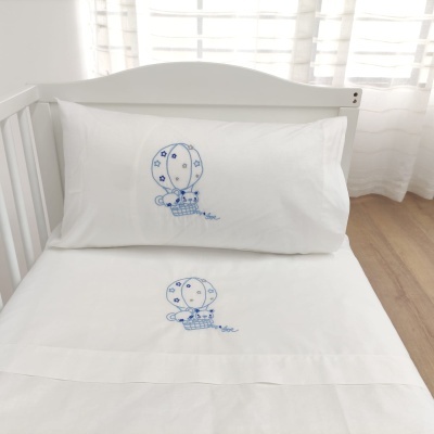 Jogo de cama infantil branco com bordado azul de balão em berço branco