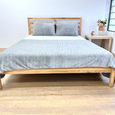 Cama de madeira clara com roupa de cama cinza e almofadas, mesa lateral com vaso de flores