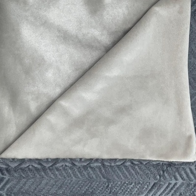 Pano cinza claro dobrado sobre tapete cinza escuro com padrão geométrico