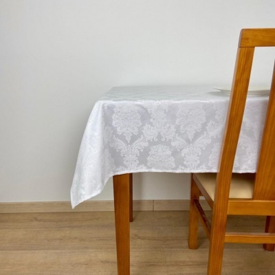 Mesa de madeira clara com toalha branca decorada e cadeira de madeira clara