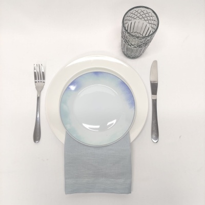 Conjunto de louça com prato pequeno colorido, guardanapo cinza, talheres e copo transparente