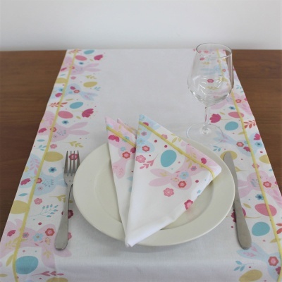 Mesa posta com toalha branca estampada, prato branco, guardanapo dobrado, talheres e copo de vidro