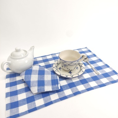 Conjunto de chá com bule branco e chávena creme azul sobre toalha azul e branca às quadrículas