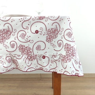 Toalha de mesa branca com padrão floral vermelho e barra franzida sobre mesa de madeira clara