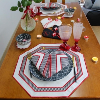 Conjunto de jantar decorativo numa mesa de madeira com pratos, talheres, copos vermelhos, guardanapos e velas.