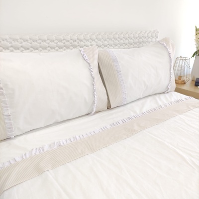conjunto de roupa de cama branca com detalhes bege e franjas, cabeceira branca trançada e mesa de cabeceira de madeira