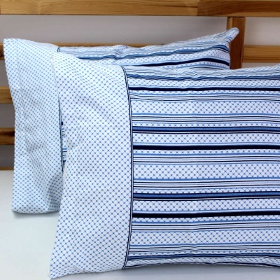 Dois fronhas de almofada com padrões azuis e brancos numa cama de madeira clara.