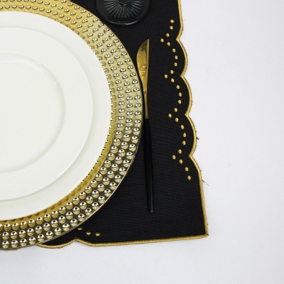 Prato branco com aro dourado e faca preta e dourada sobre individual preto com borda dourada