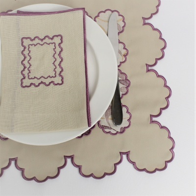 Jogo de mesa em tecido bege com bordas roxas onduladas, guardanapo dobrado em prato branco com faca ao lado.