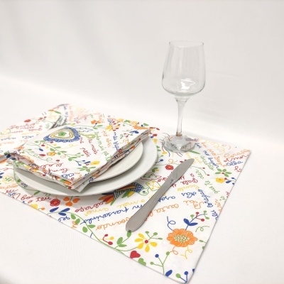 Jogo americano e guardanapos brancos com padrão colorido floral e palavras, prato branco, faca e copo de vinho