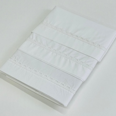 Lençol branco dobrado com bandas decorativas e detalhes em renda