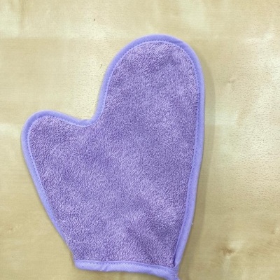 Luva de banho lilás de tecido felpudo com alça, sobre superfície de madeira clara